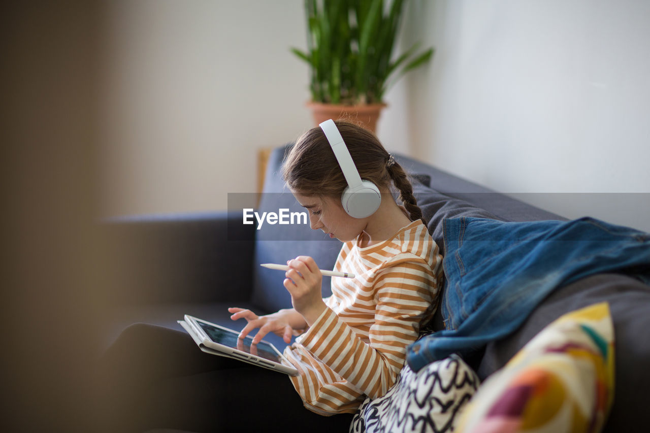 Side view of girl using digital tablet while sitting on sofa