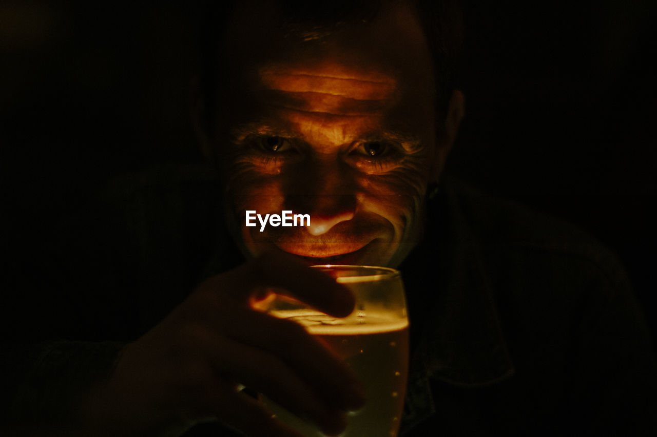 Close-up portrait of smiling man holding alcoholic drink against black background