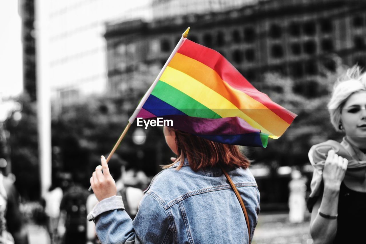 REAR VIEW OF WOMAN HOLDING MULTI COLORED UMBRELLA