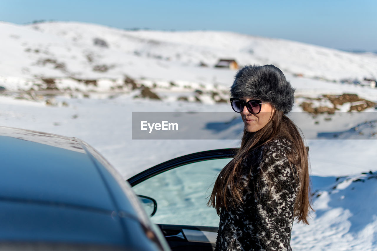 Portrait of woman standing by car on snow covered land