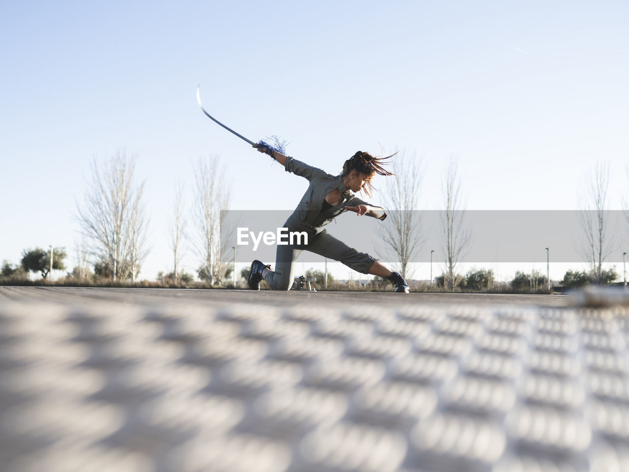 Young woman with sword practicing martial arts in park against clear sky