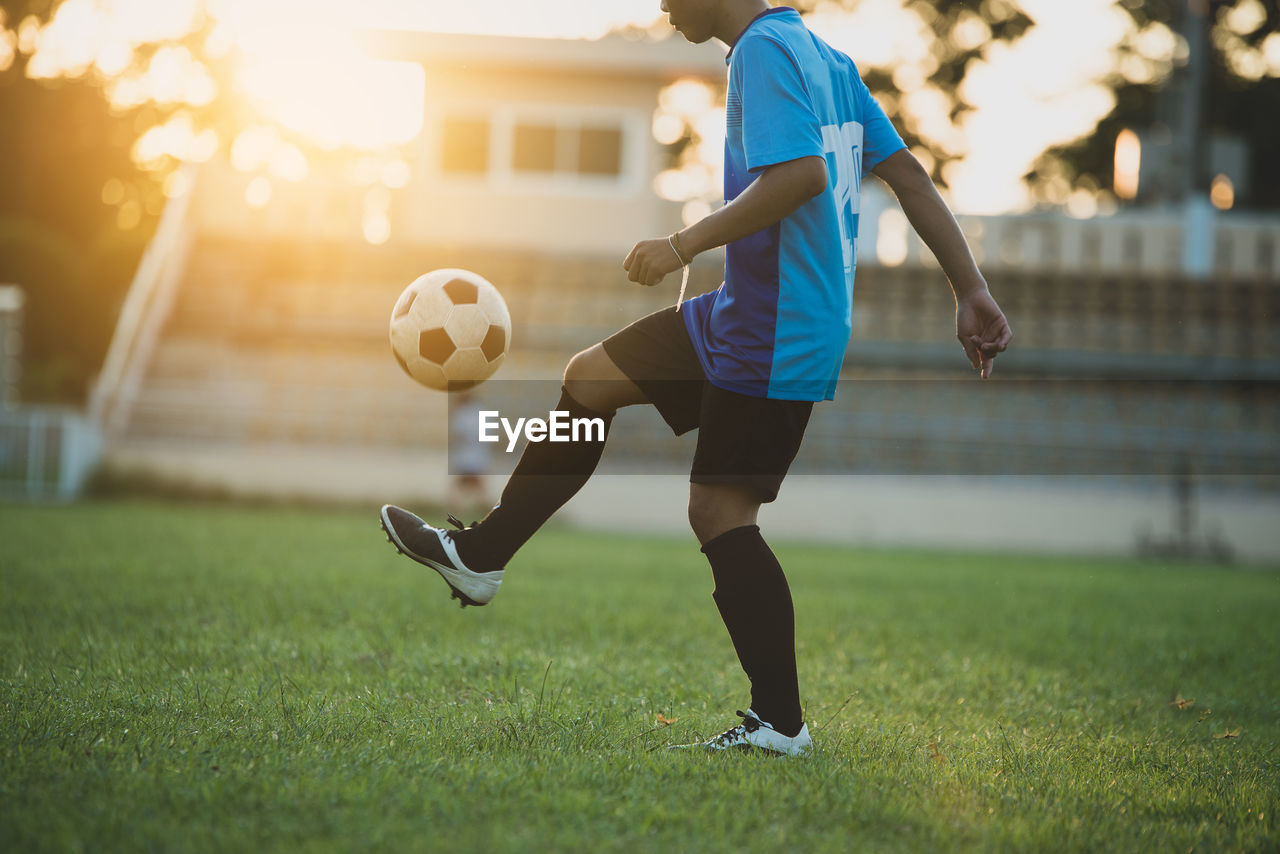 FULL LENGTH OF WOMAN PLAYING SOCCER BALL ON GRASS