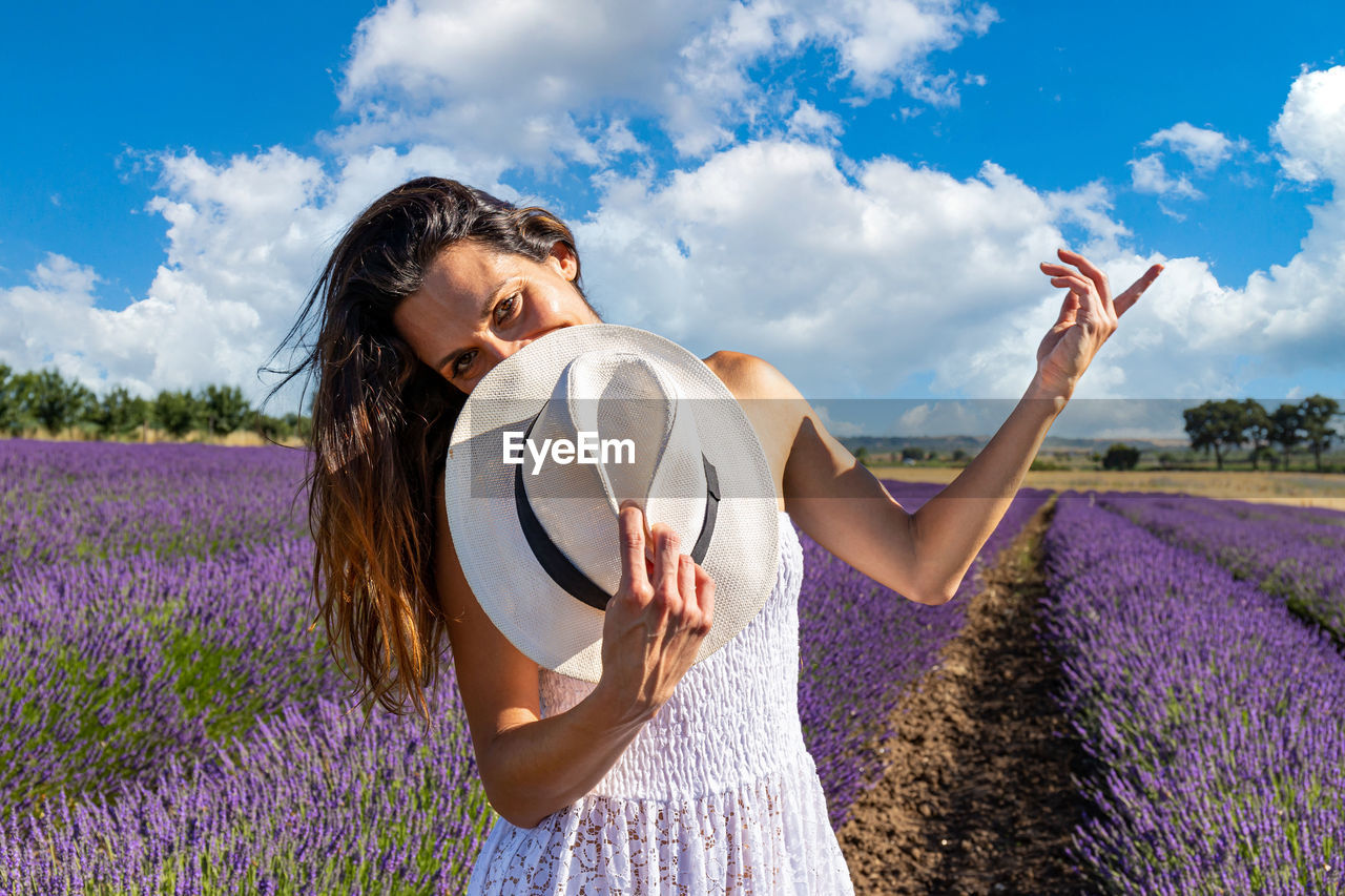 Happy young woman playing with her hat in a blooming lavender field. 