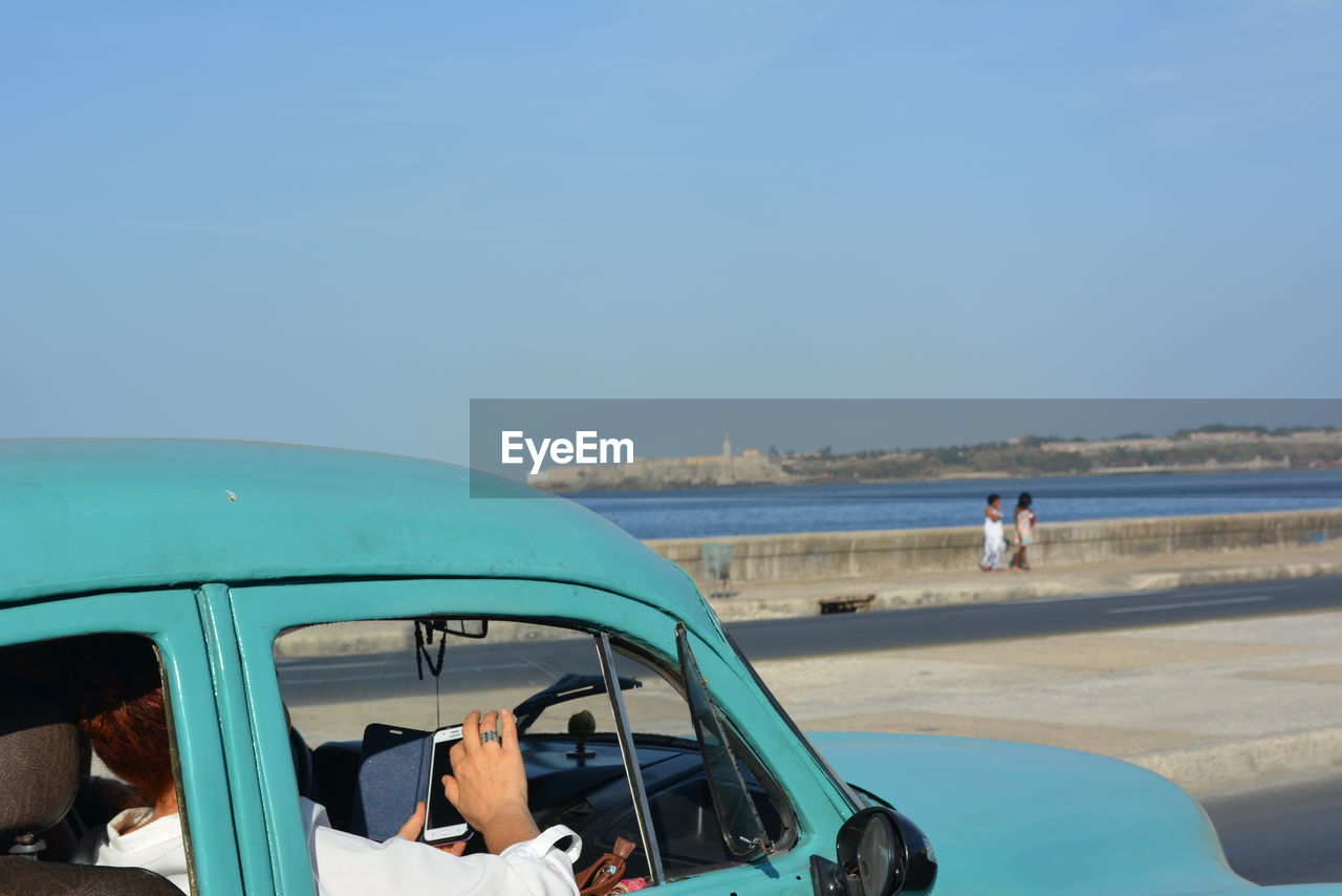 Woman holding mobile phone in old-fashioned blue car on road