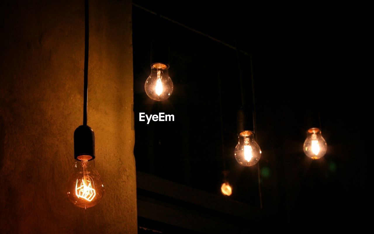 Close-up of illuminated light bulb hanging at night