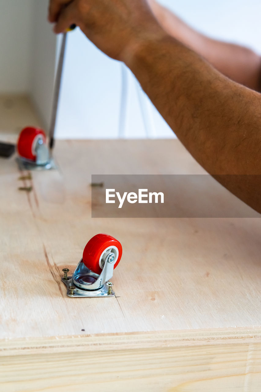 Close-up of electrical screwdriver fixing castor wheel on a wooden table.