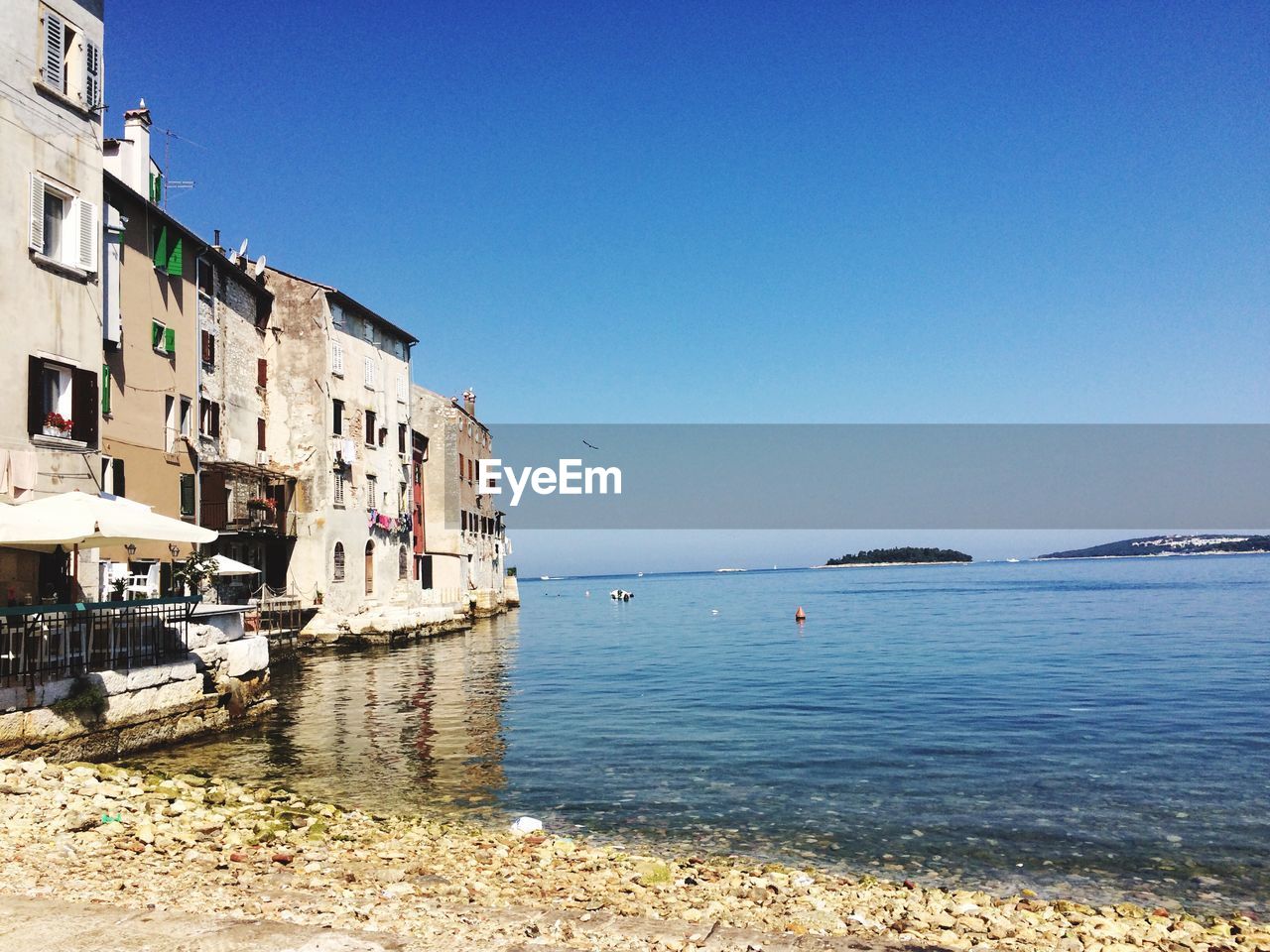 Buildings by sea against clear blue sky