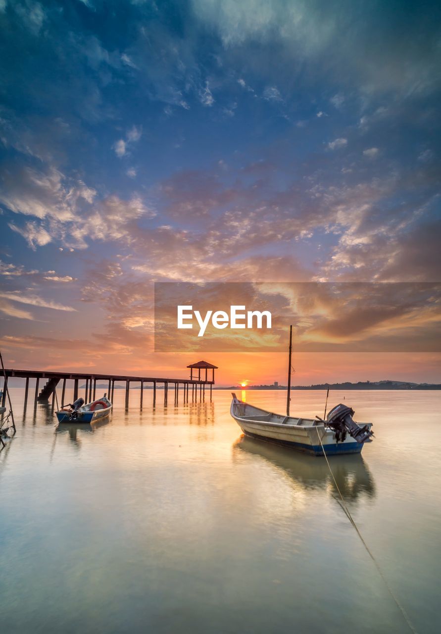 Boat moored in sea against sky during sunset