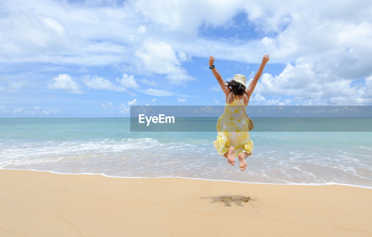 Excited energetic happy tourist girl is jumping at the beach on summer vacations,