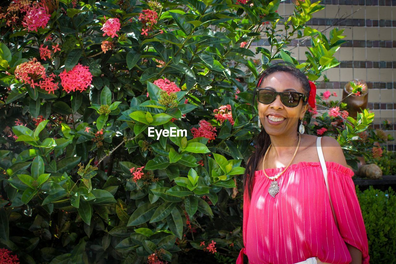 Portrait of smiling mature woman wearing sunglasses standing by plants