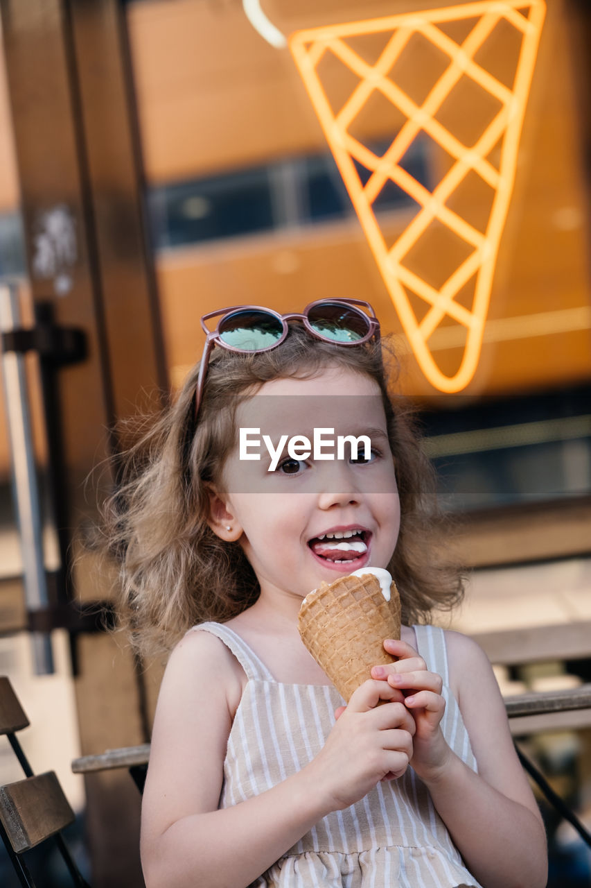 Toddler child eating cone ice cream outside near cafe. cute blonde caucasian girl licking frozen