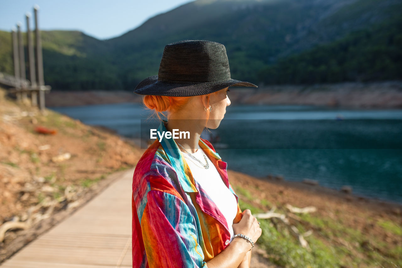 Side view woman in a lake, looking away with one hand holding a black hat