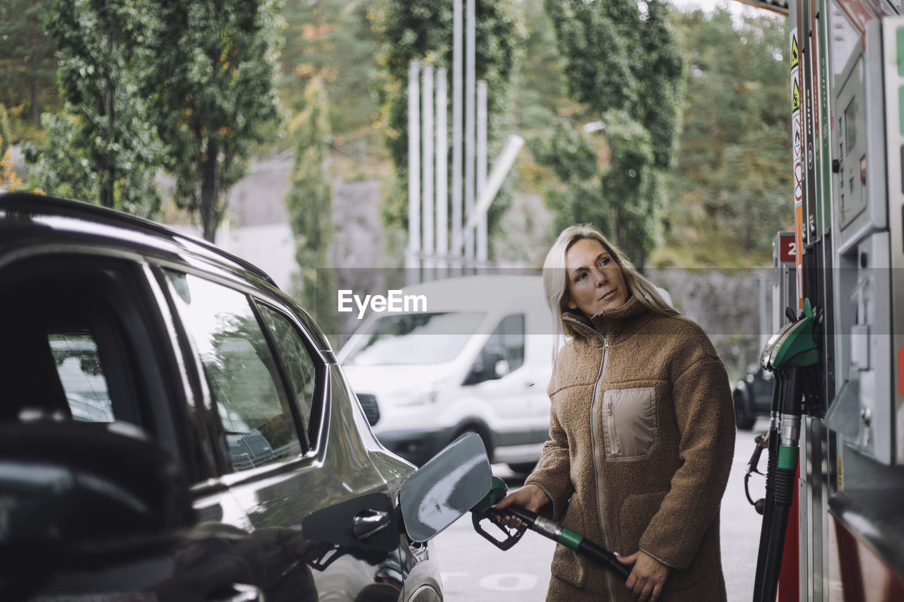 Mature woman pumping gas in car while standing at fuel station