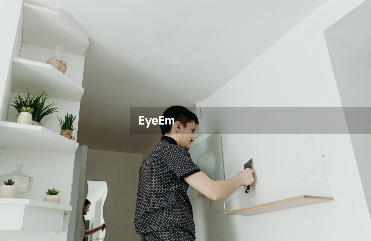 A young man covers a hole in the wall with putty with a spatula.