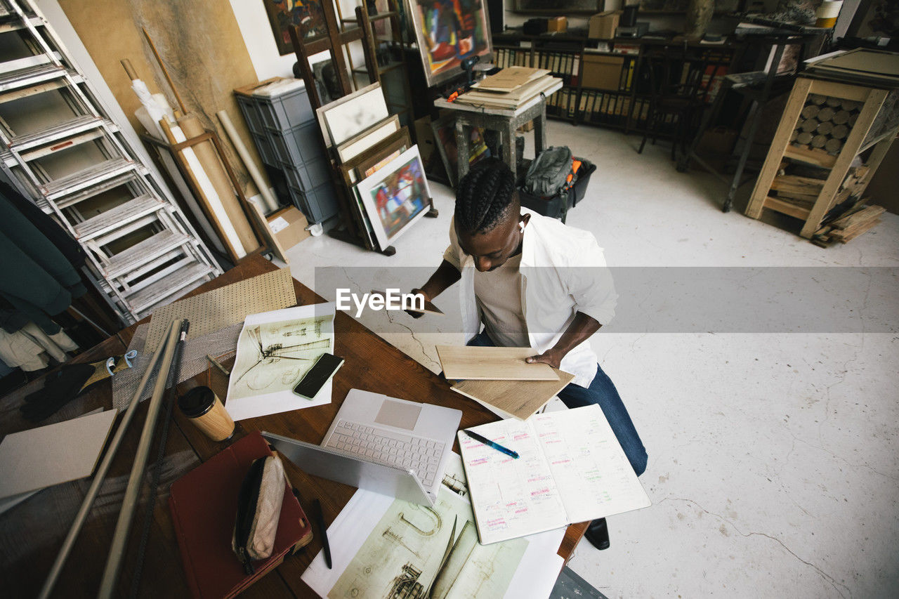 Directly above shot of male architect examining wooden swatch while sitting in workshop