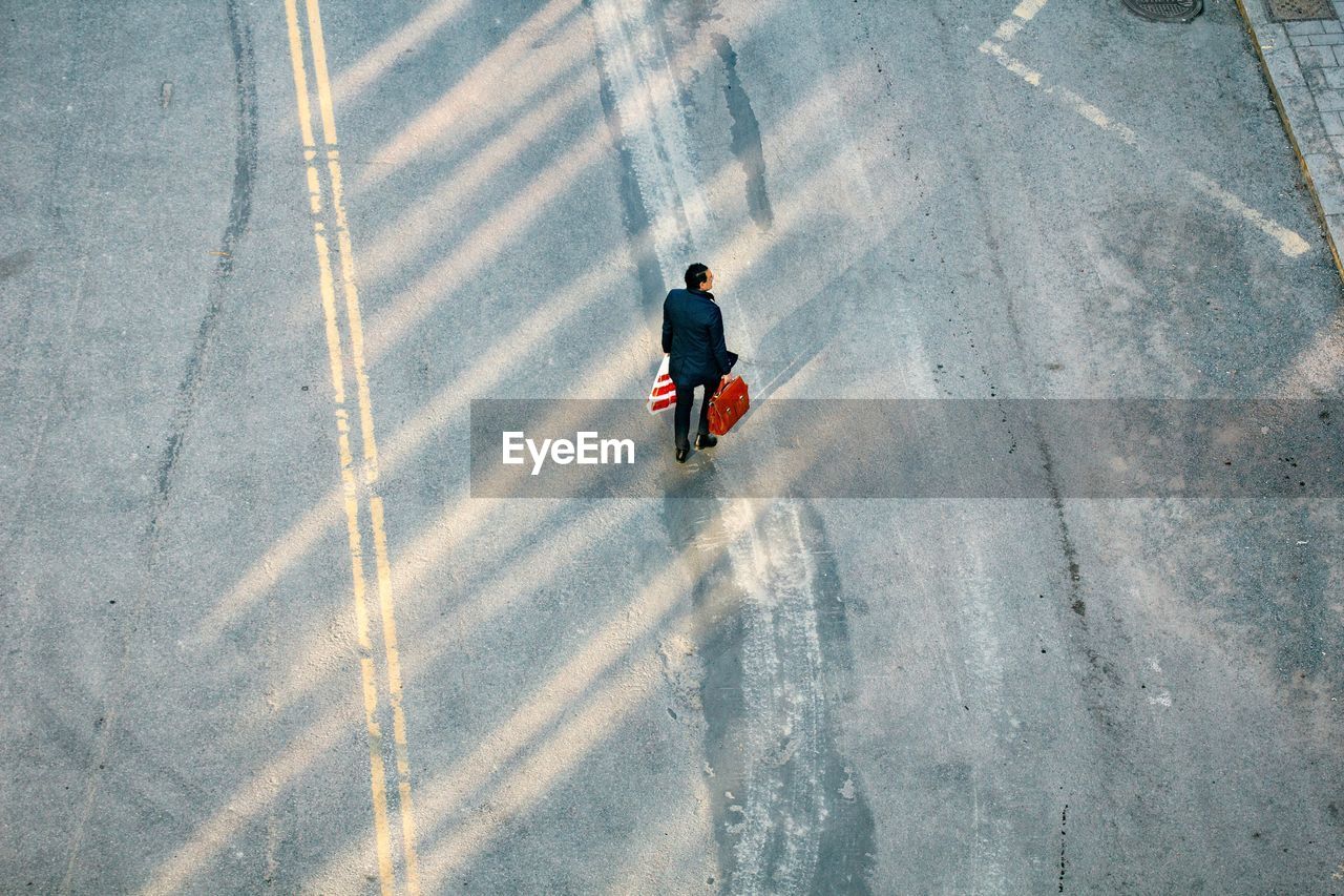 FULL LENGTH REAR VIEW OF MAN WALKING ON ROAD IN CITY