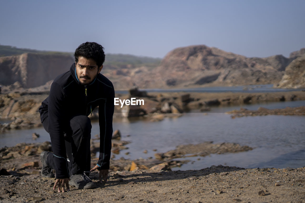 Young indian fit boy jogging in the morning near a lake situation in middle of a mountain area.