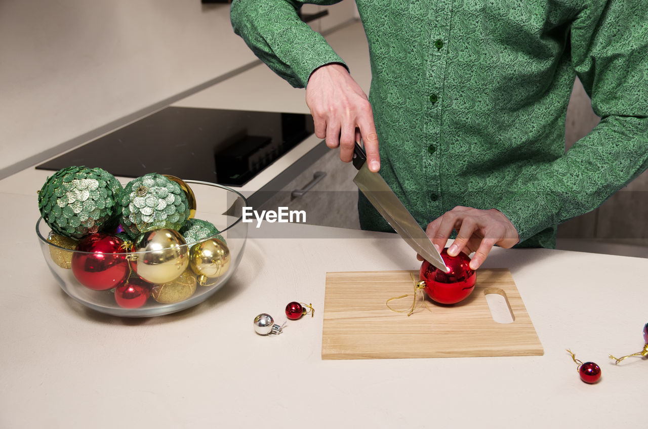 Man with knife in his hand cuts salad of decorated christmas balls