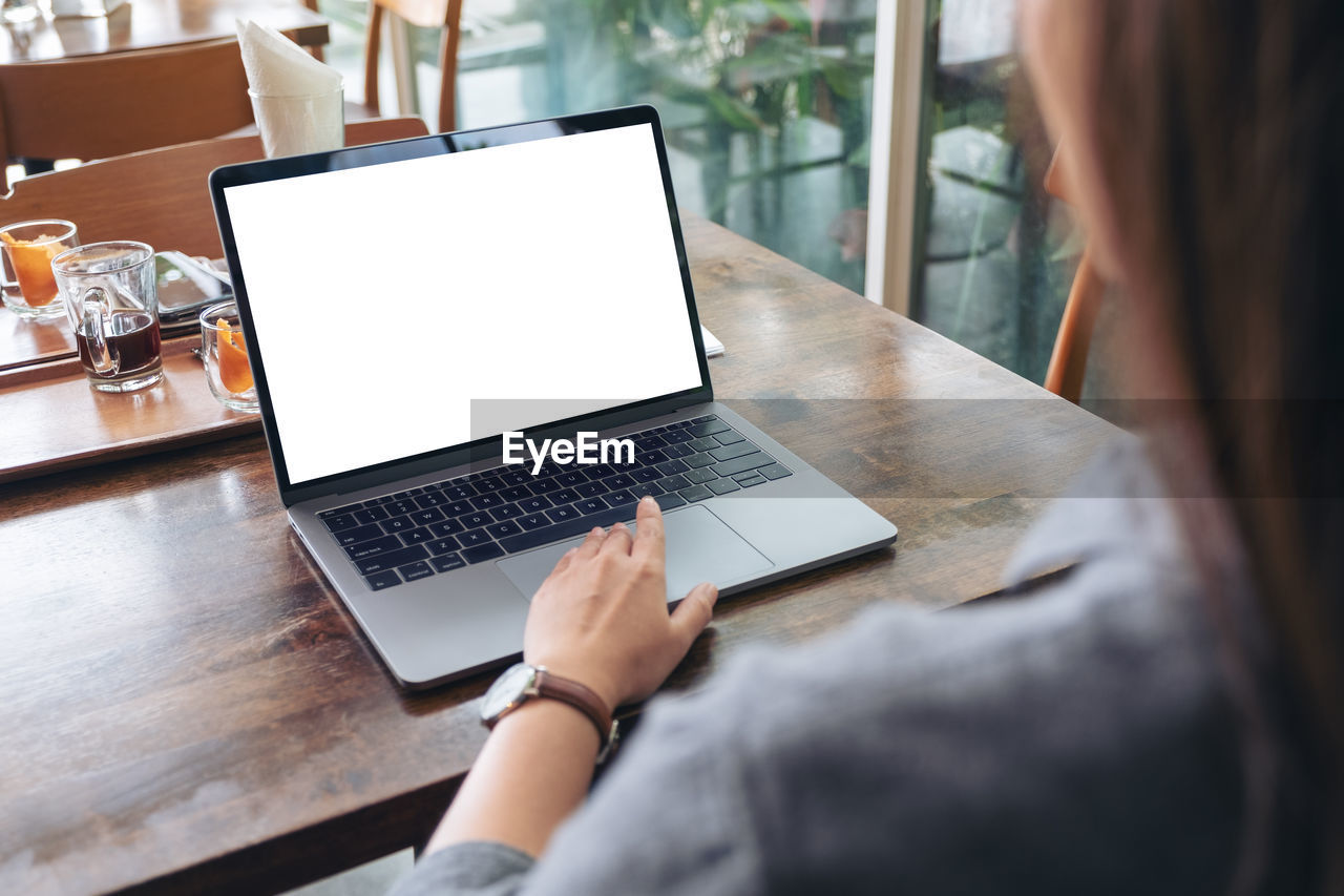 Midsection of woman using laptop at cafe