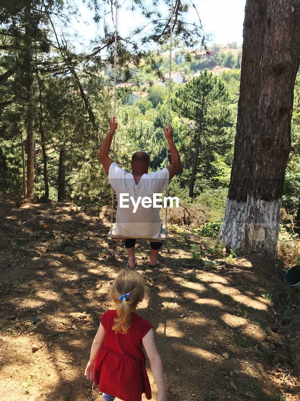 Man swinging with daughter in forest