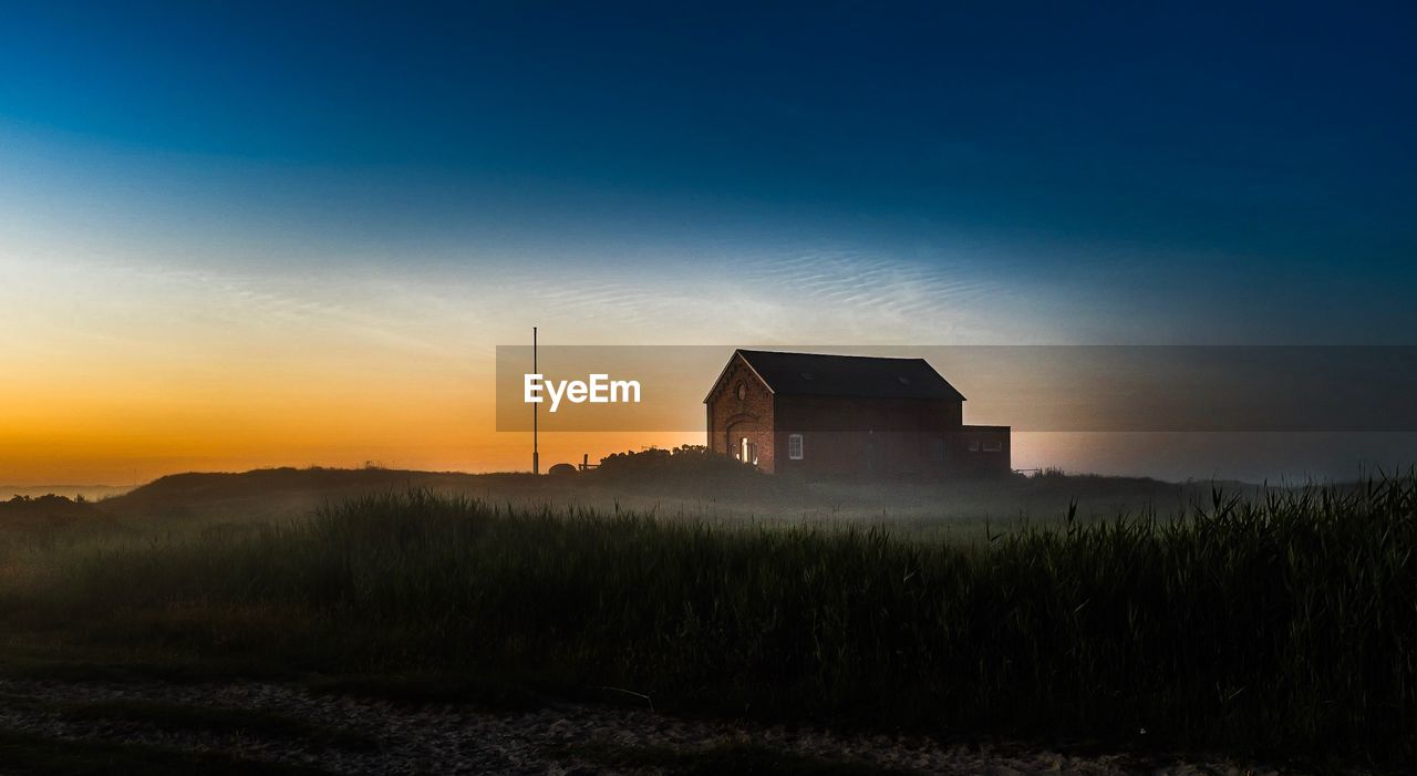 Silhouette house on field against sky during sunset