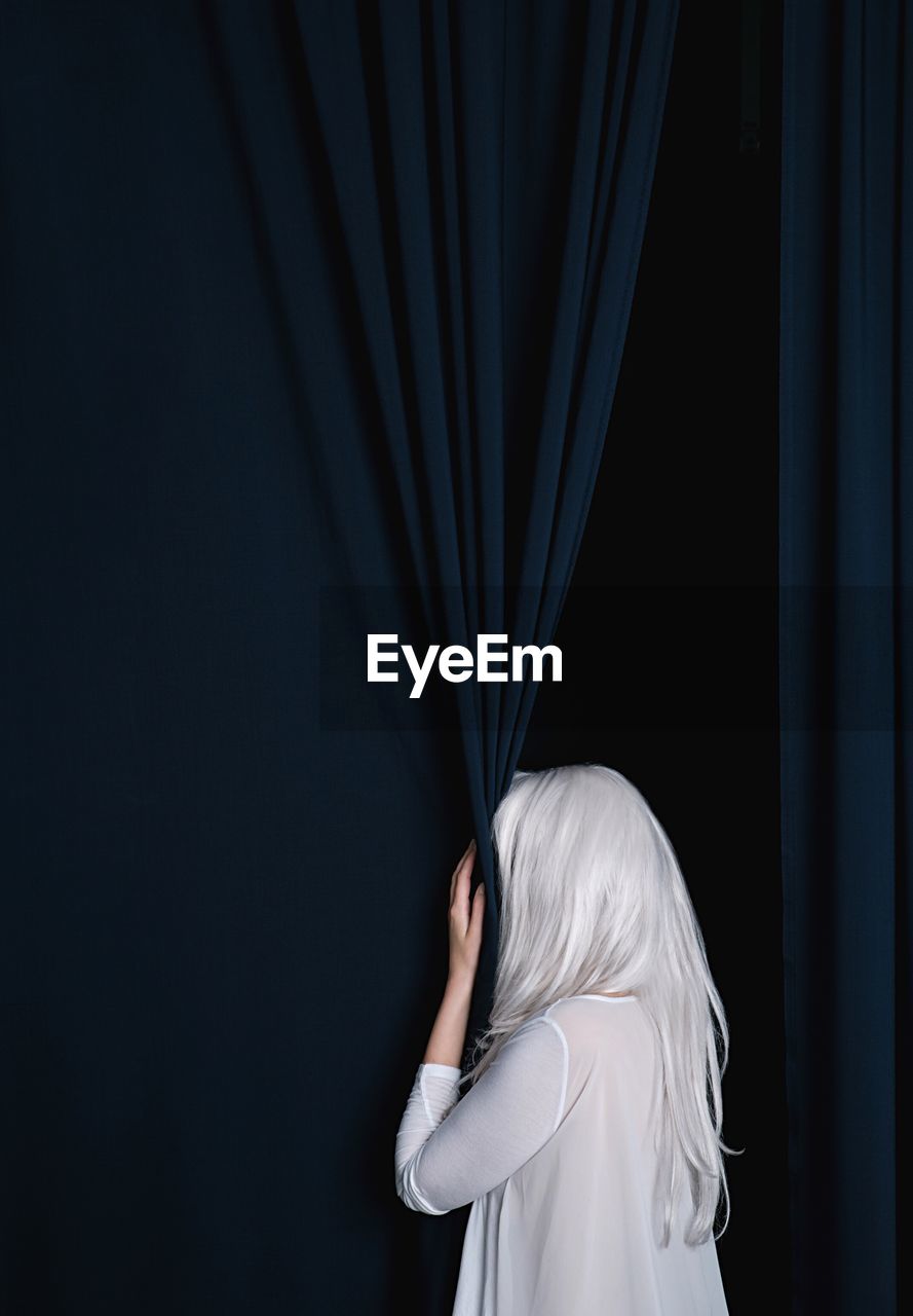 Rear view of woman hiding by curtain