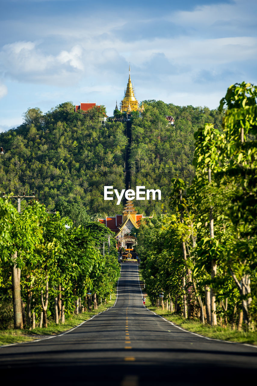 Diminishing perspective of road amidst trees leading towards temple against sky