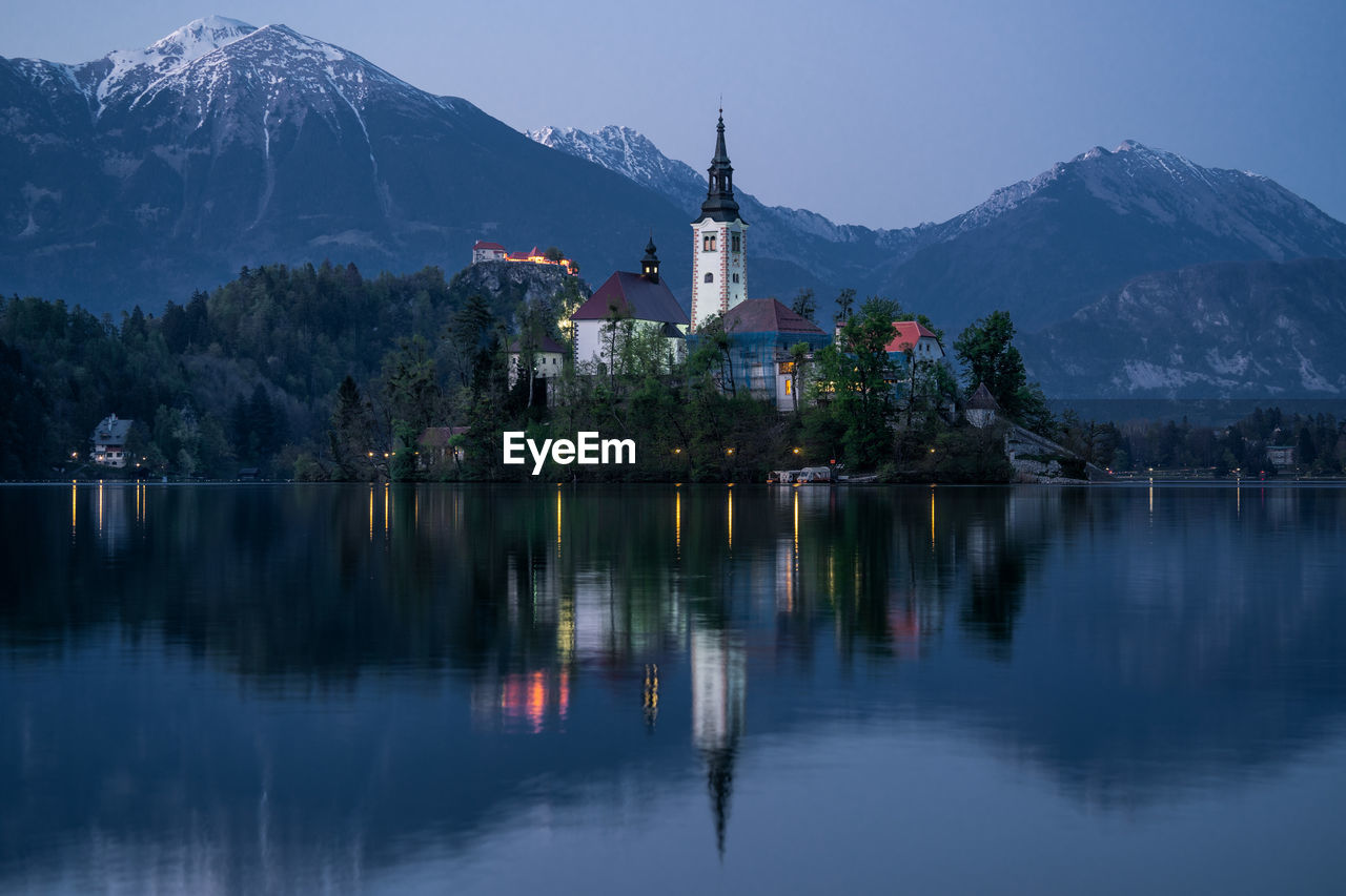 SCENIC VIEW OF LAKE BY BUILDINGS AGAINST MOUNTAIN