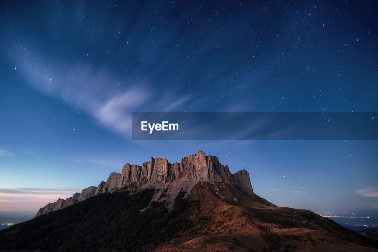 Twilight panoramic mountain view, starry sky and clouds, city lights in the background