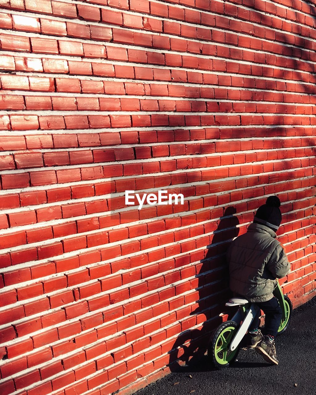 Boy riding bicycle by brick wall