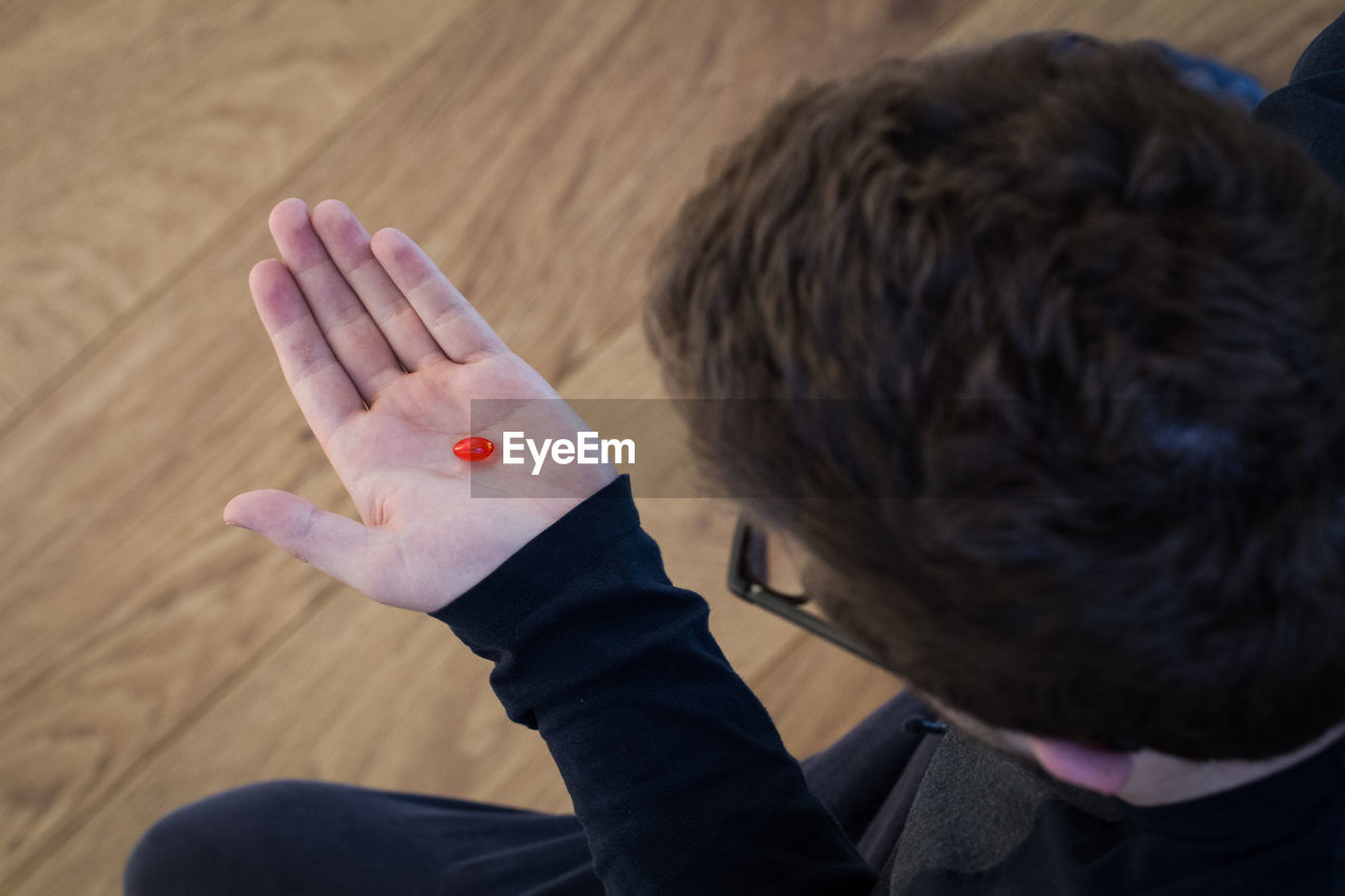 High angle view of man having pill while sitting on hardwood floor