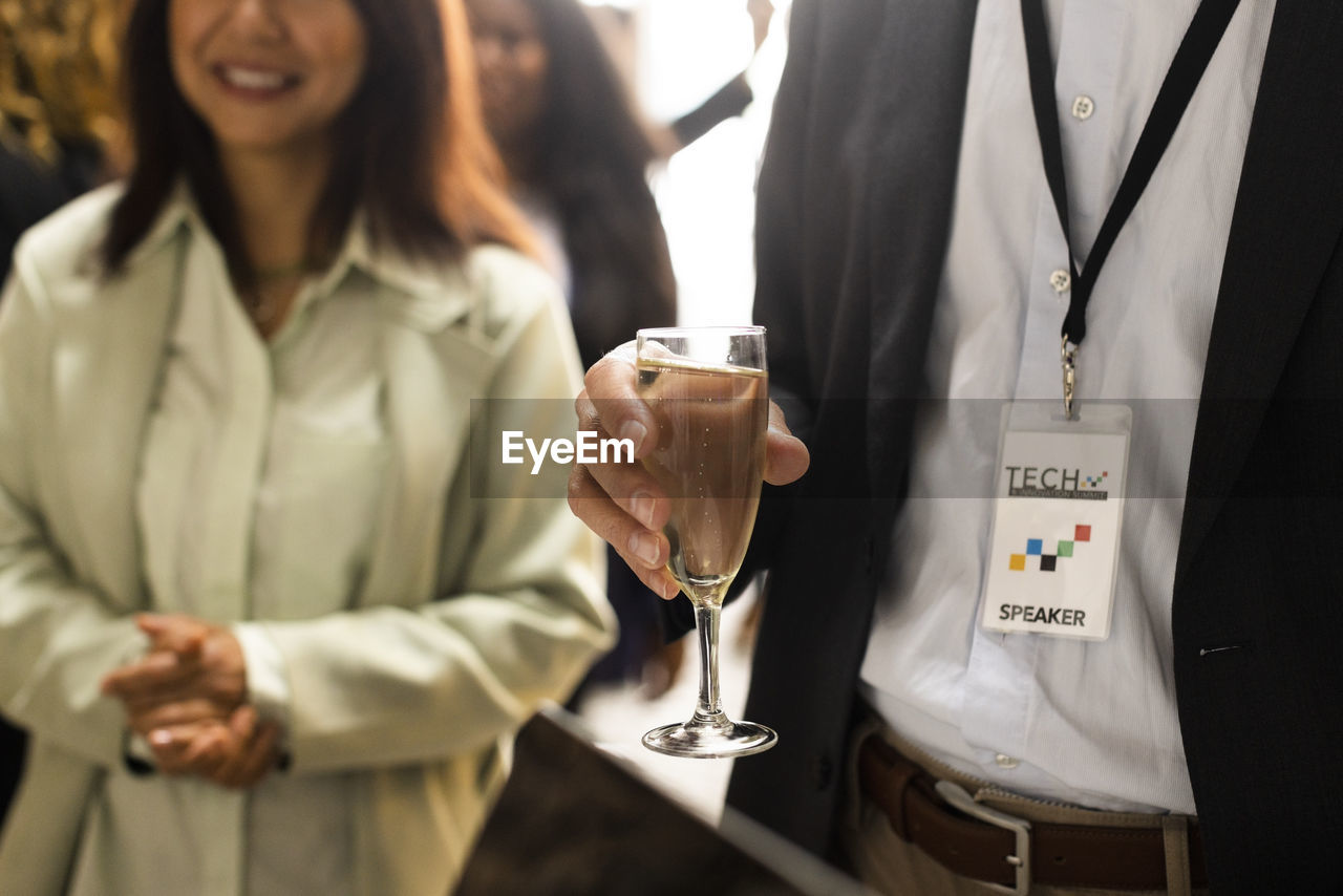 Midsection of businessman with wineglass standing by female colleague during corporate event