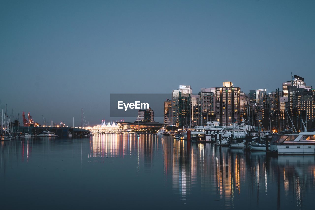 Illuminated buildings by sea against clear sky at night