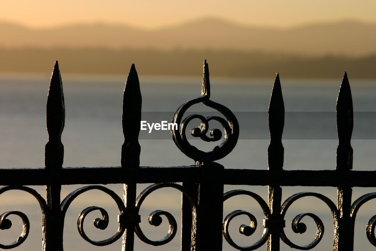 Close-up of metal fence against sky during sunset