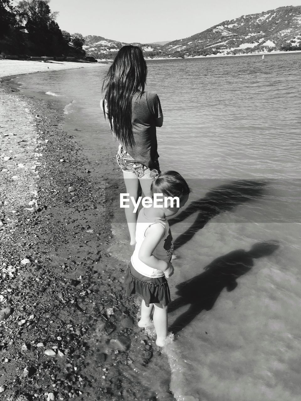 Rear view of young woman with girl standing at lakeshore