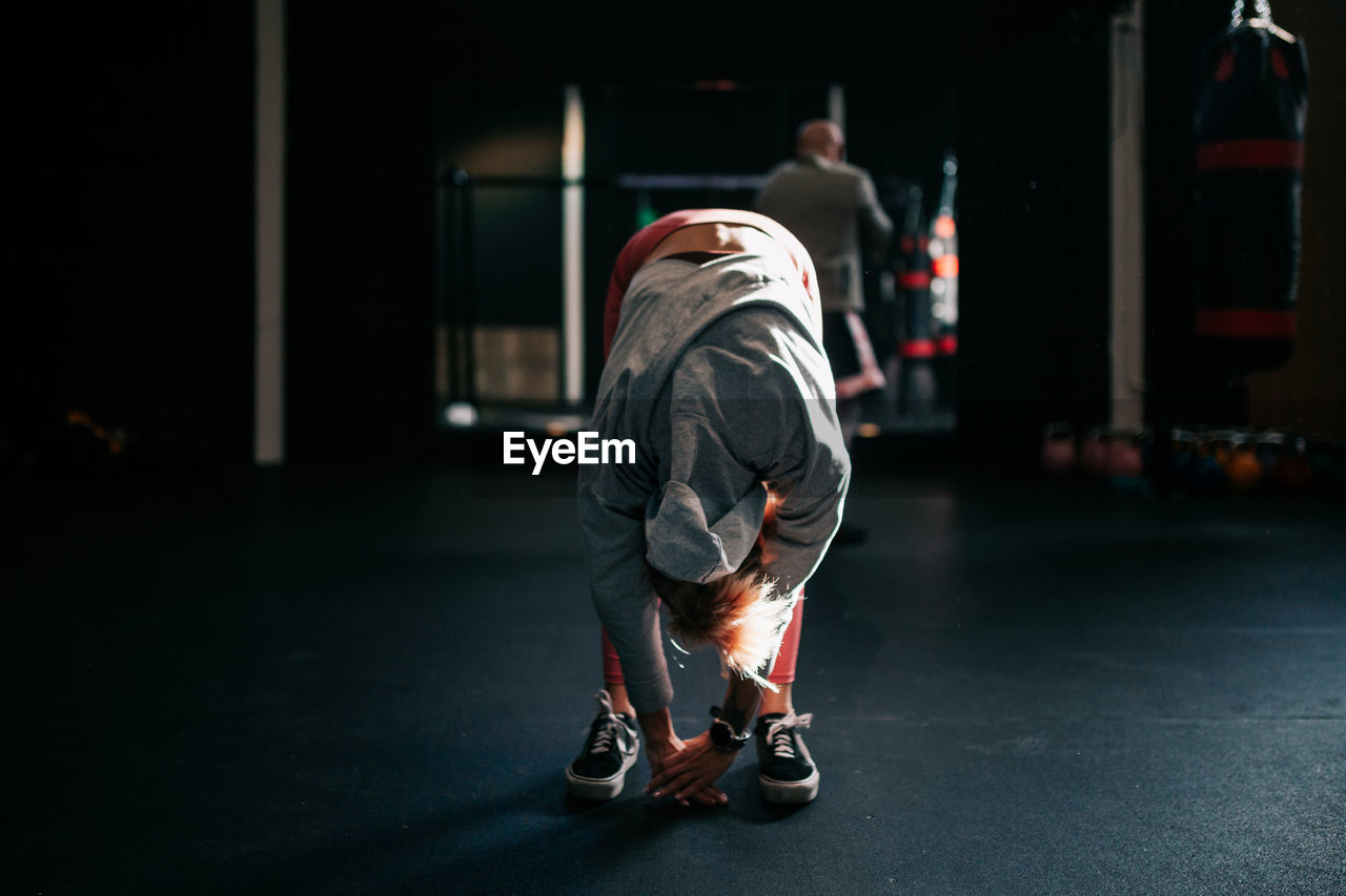 Powerful unrecognizable female boxer doing bend down exercise during intense workout in modern center