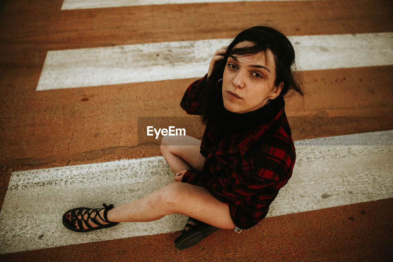 Portrait of young woman sitting on zebra crossing