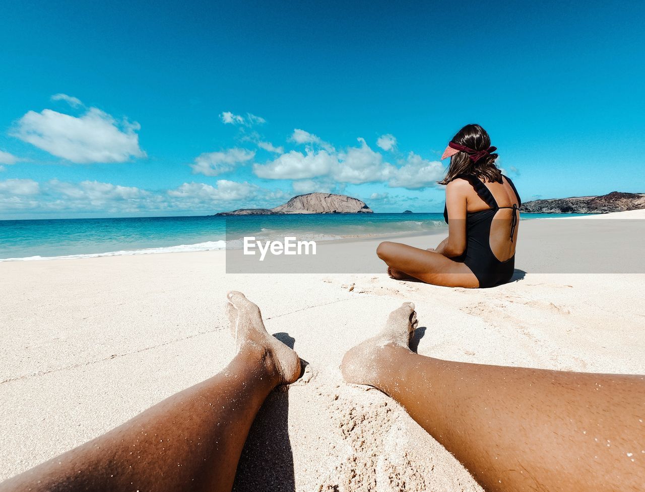 REAR VIEW OF WOMAN SITTING ON BEACH