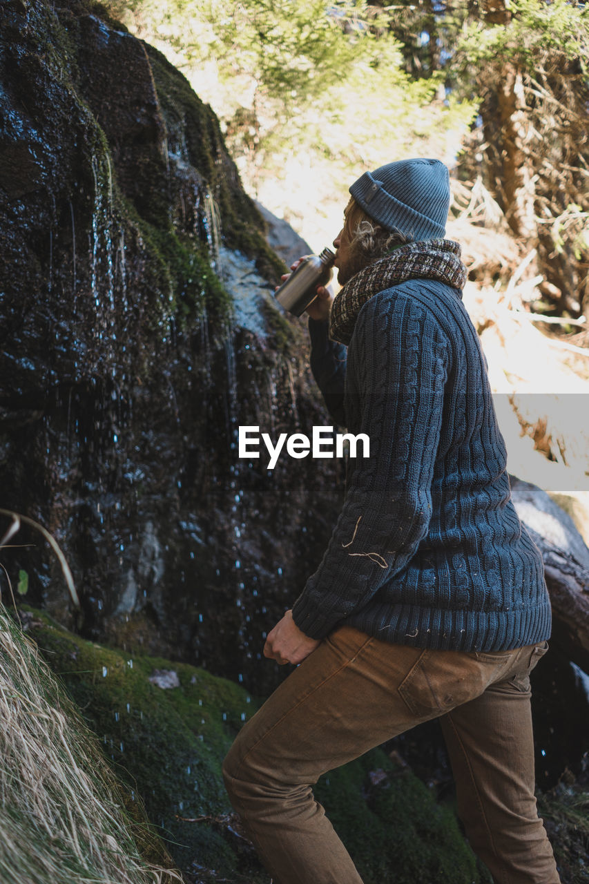 Side view of man drinking water by rock formation