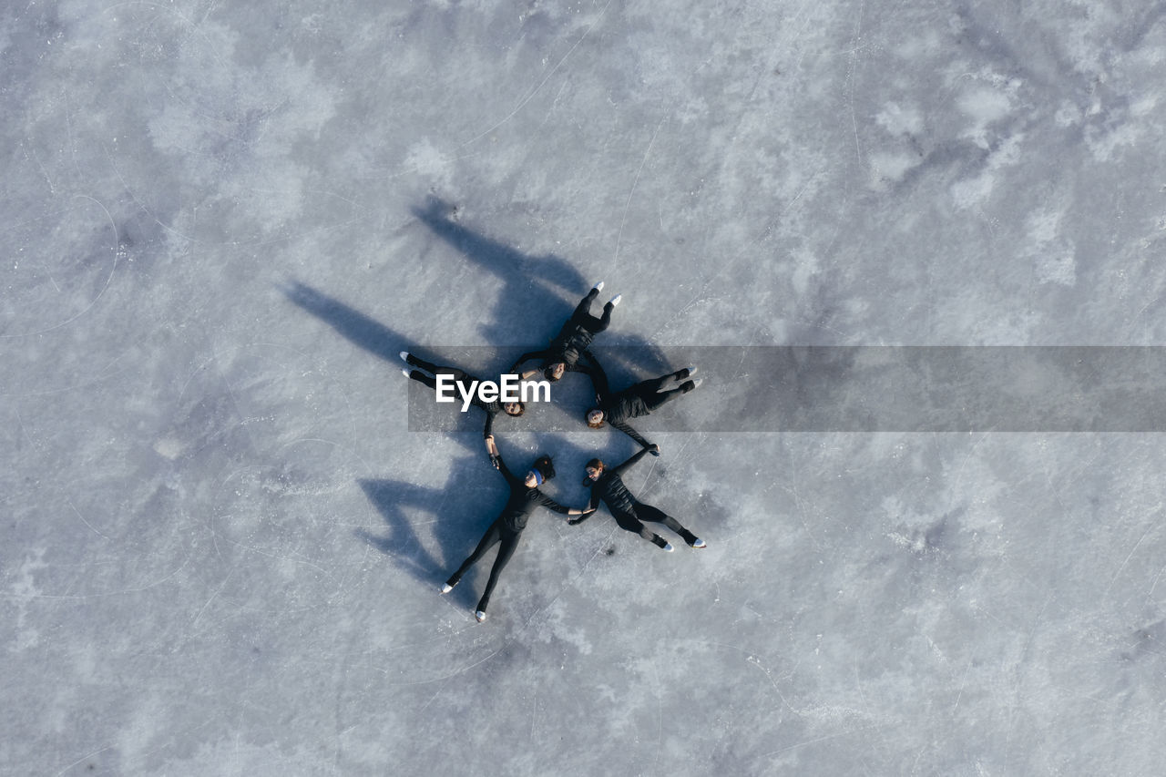 Aerial view of group of female ice-skaters lying together on surface of frozen lake