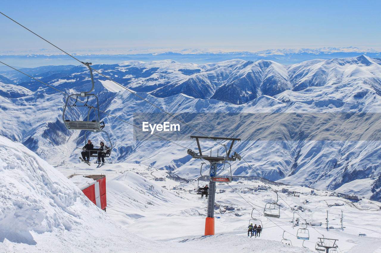 Chairlift with skiers on the background of snowy peaks and blue sky