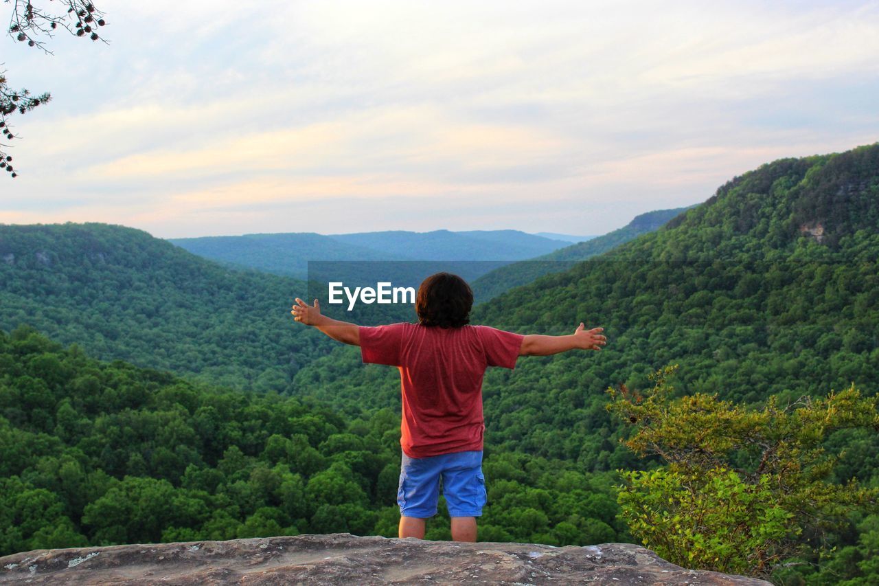 Rear view of man with arms outstretched standing on mountain against sky