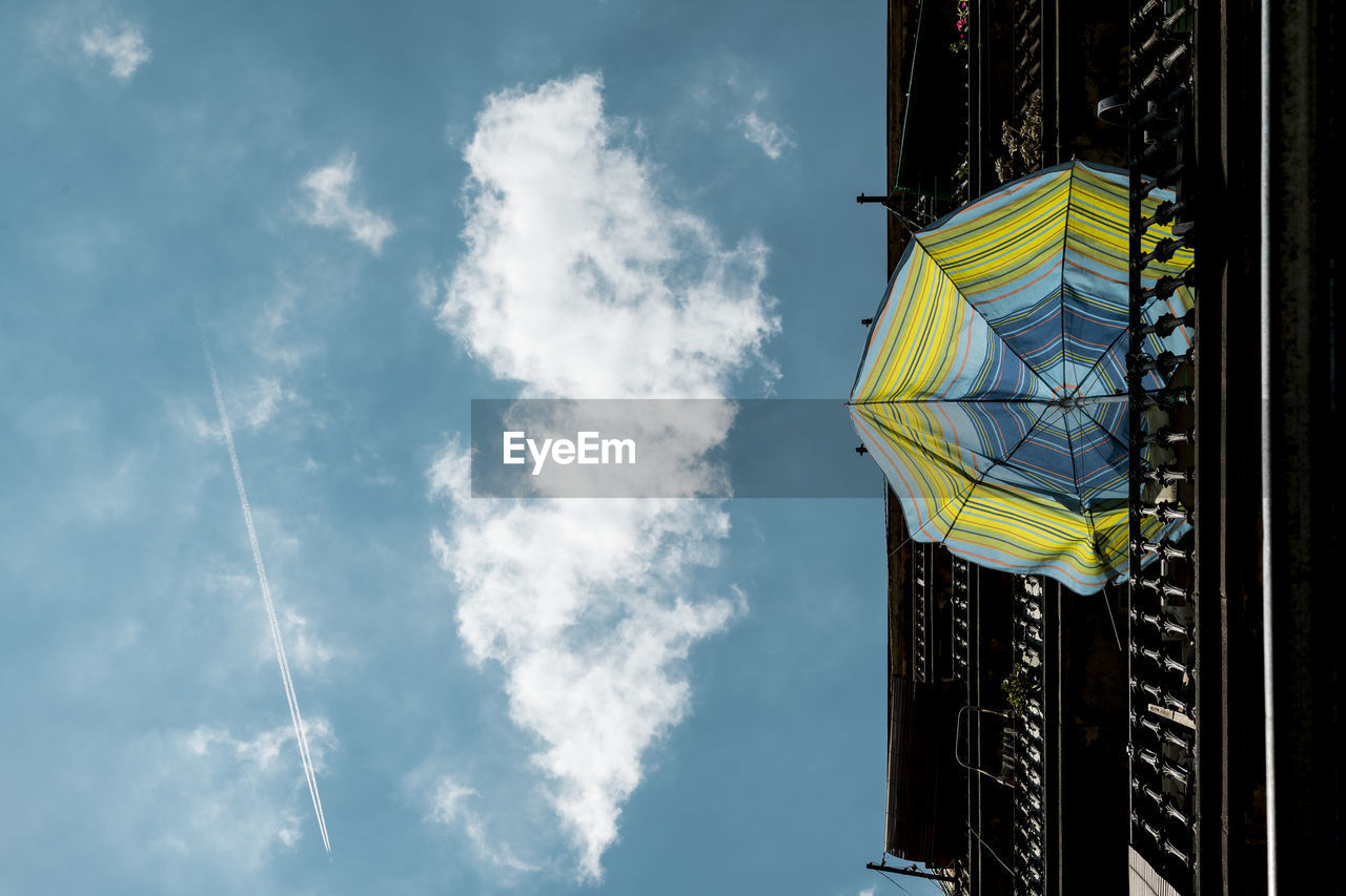 Low angle view of umbrella hanging on railing against blue sky