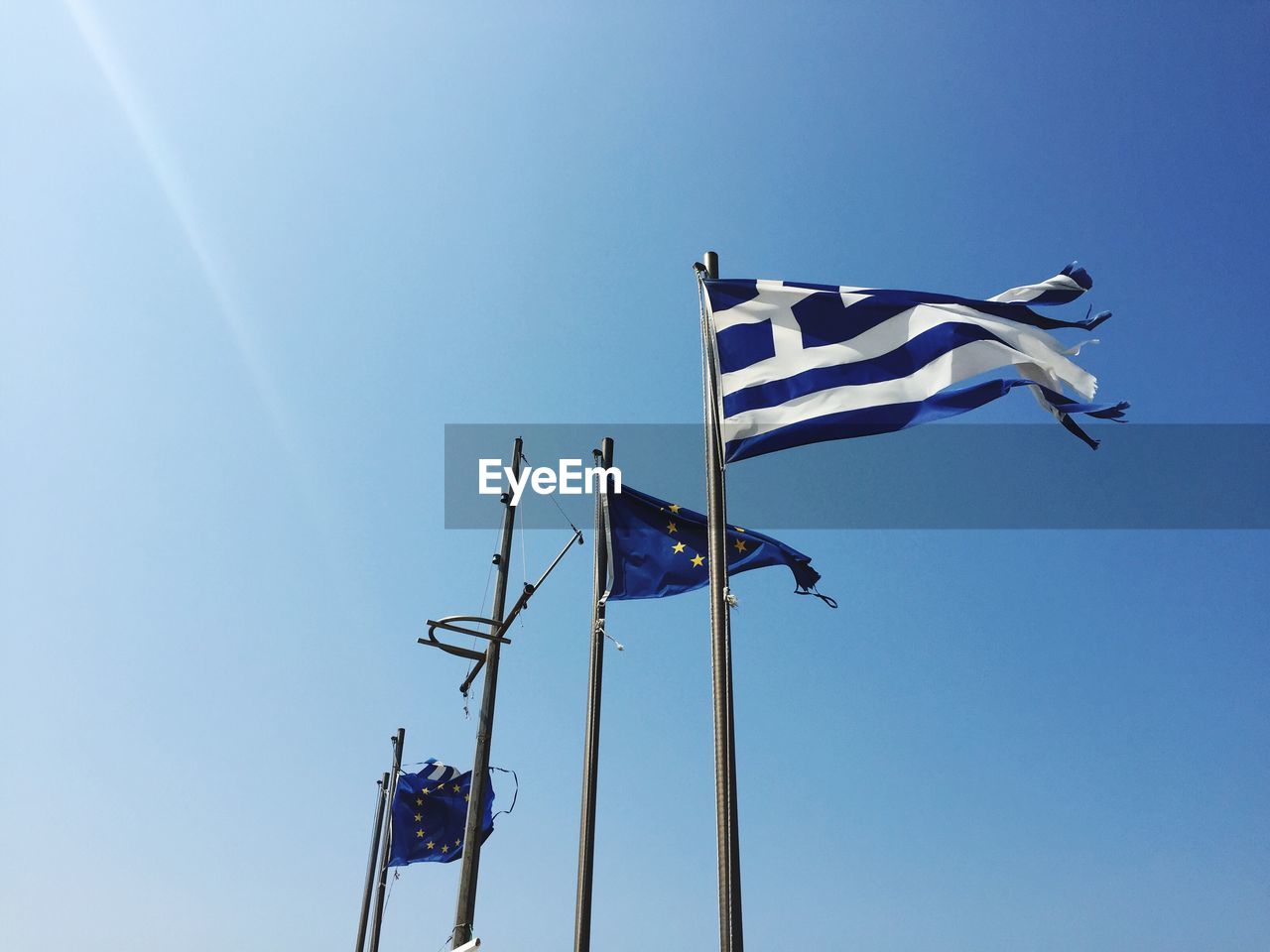 Low angle view of greek and european flags against clear blue sky