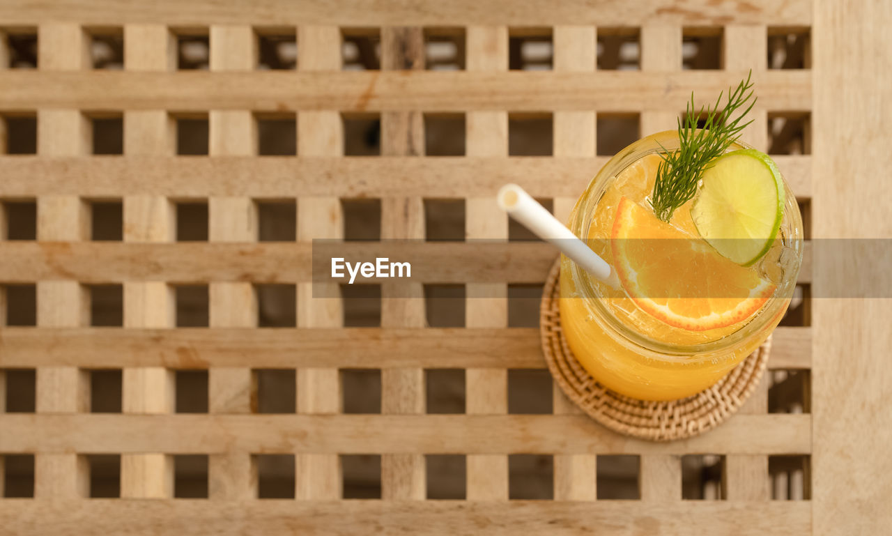 CLOSE-UP OF DRINK ON GLASS TABLE AGAINST ORANGE WALL