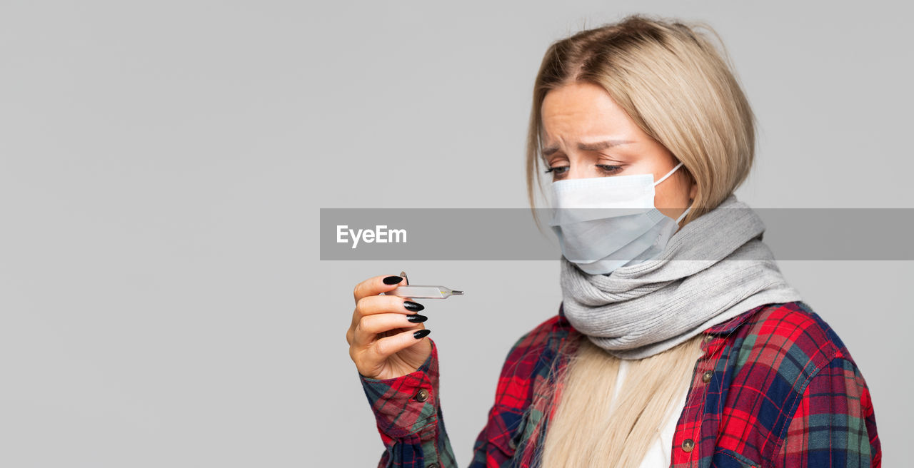 Woman wearing mask holding thermometer against white background