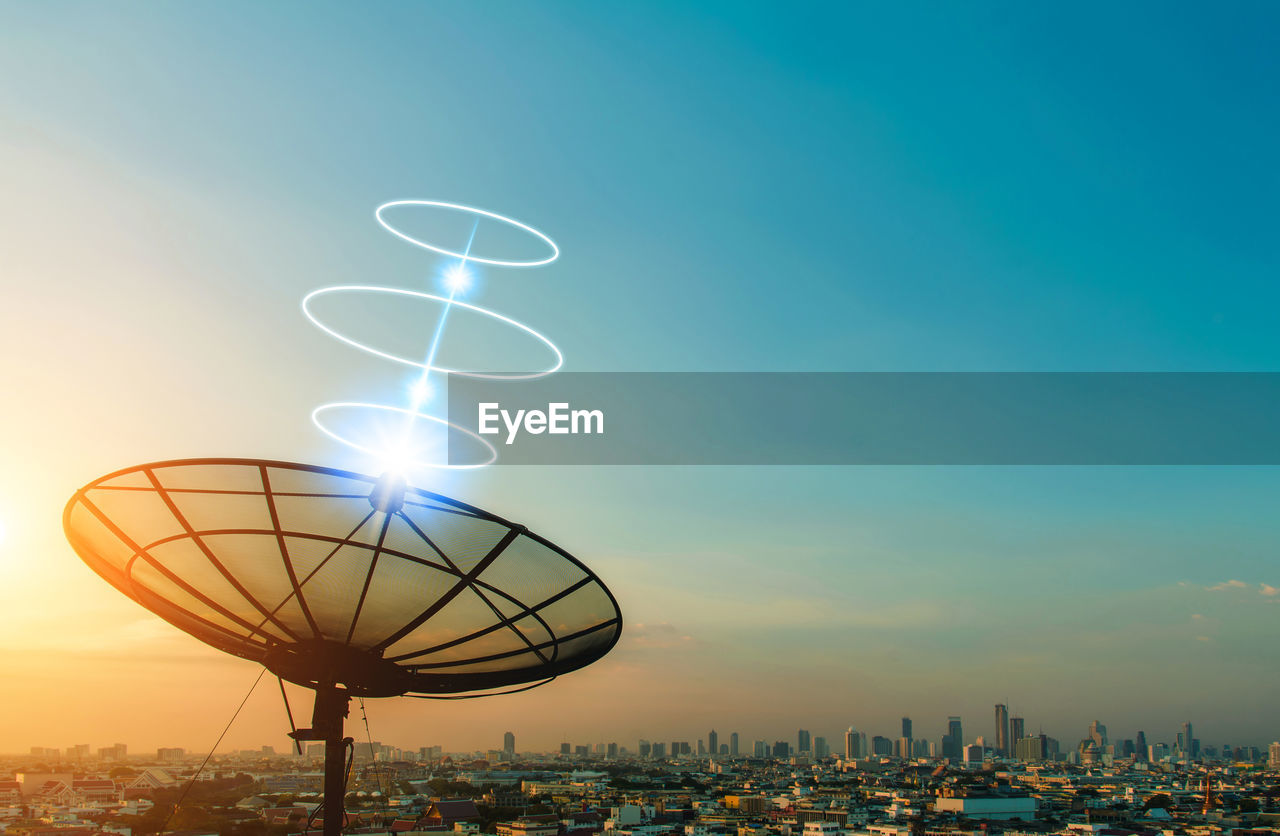 ILLUMINATED FERRIS WHEEL BY BUILDINGS AGAINST SKY