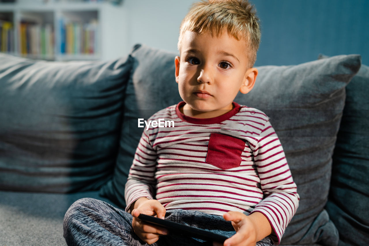 Portrait of boy holding mobile phone while sitting on sofa at home