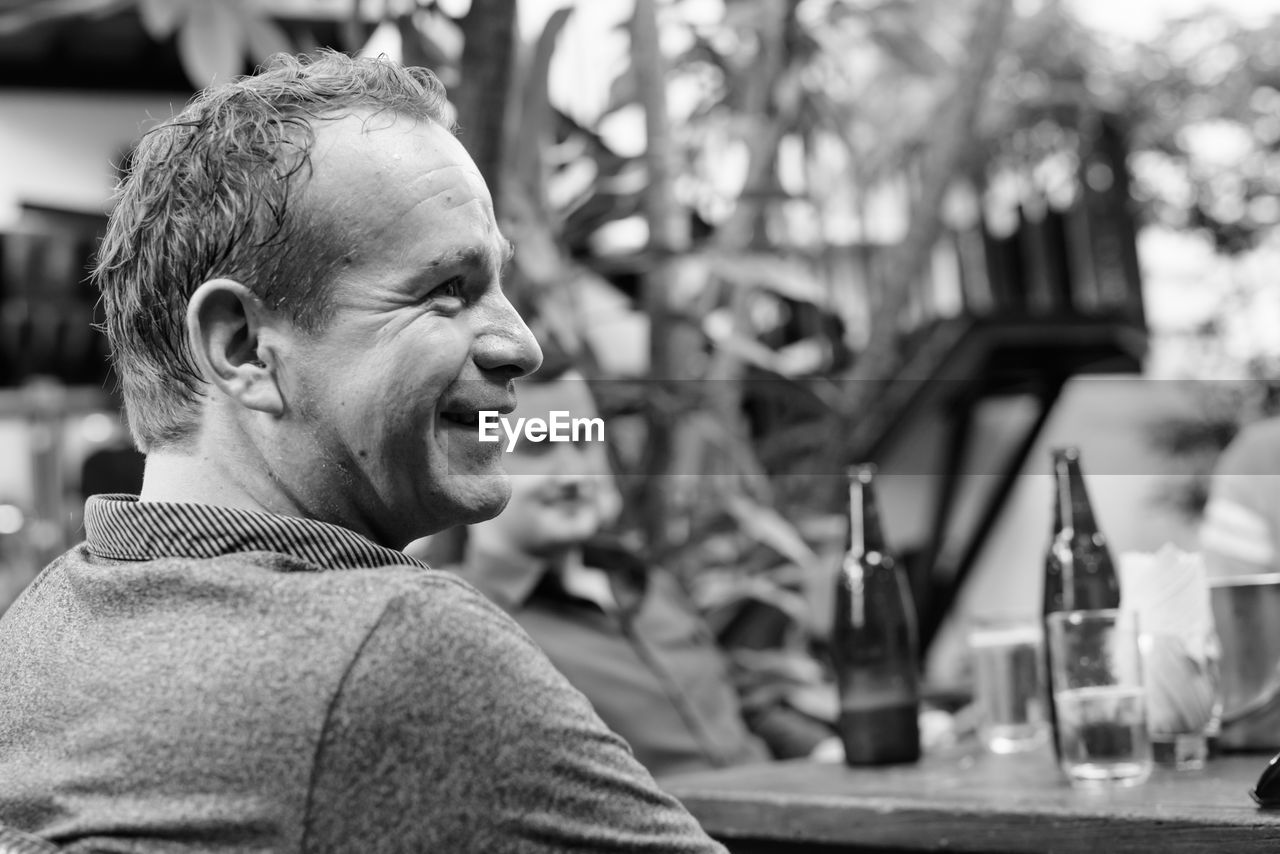 Smiling man looking away while sitting outdoors with friend