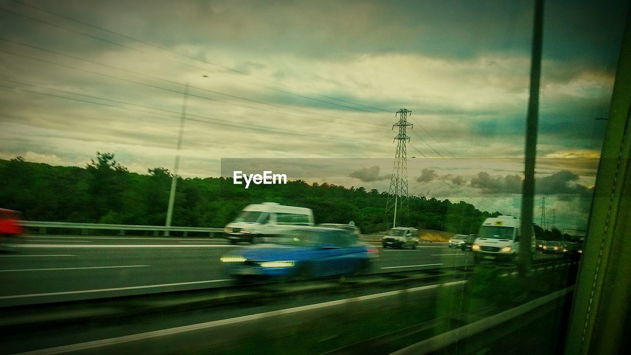 CARS ON ROAD AGAINST CLOUDY SKY